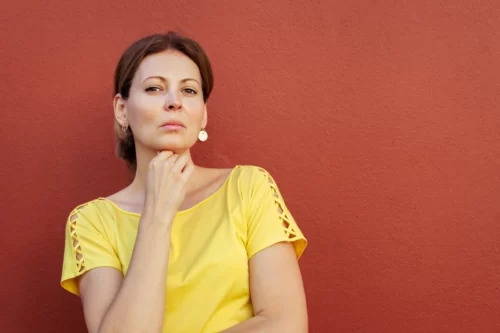 Femme en chemise jaune sur fond rouge, exprimant confiance et potentiel arrogance, illustrant la complexité de l'ego
